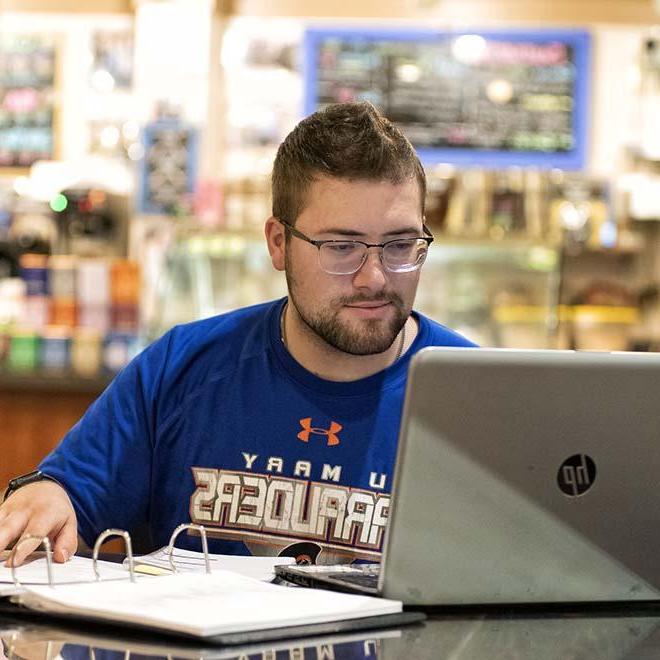 Male adult student in coffee shop studying on laptop